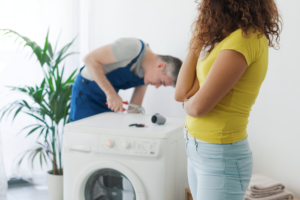 Vrouw kijkt hoe monteur haar wasmachine repareert en maakt zich zorgen om de kosten